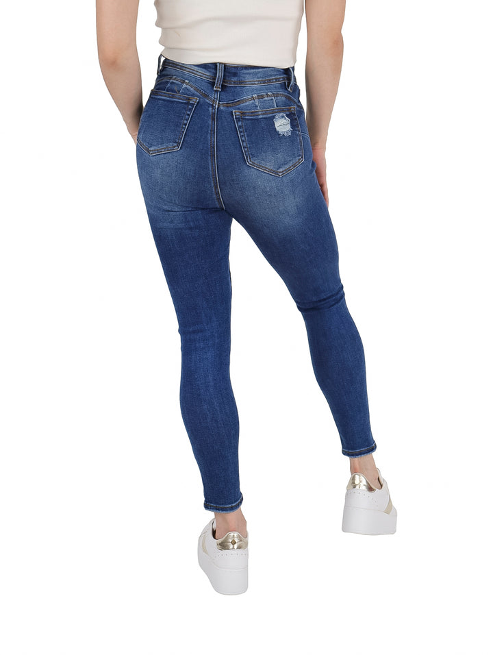 Mujer vistiendo pantalones jeans azules ajustados con detalles de destrucción en las piernas.