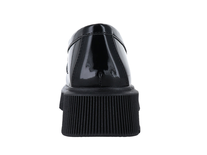 Mocasín negro brillante con suela de plataforma gruesa y adorno de cadena en la parte superior.