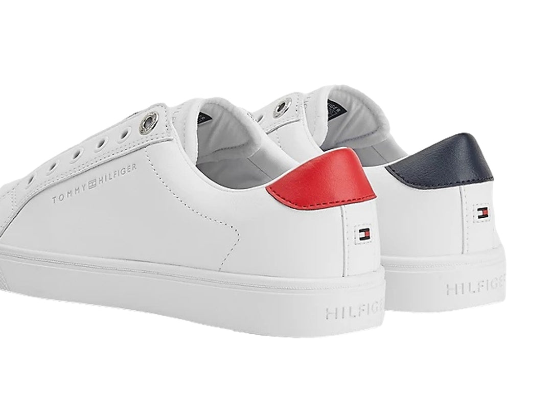 Tenis Tommy Hilfiger blancos estilo slip-on con banda elástica tricolor y detalle rojo en el talón.