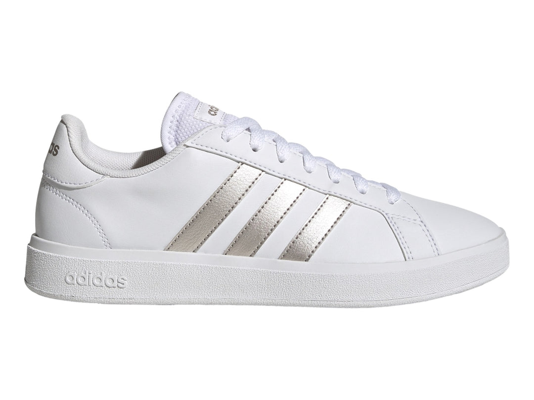 Tenis Adidas blancos con franjas laterales en color plata metálico y suela blanca.