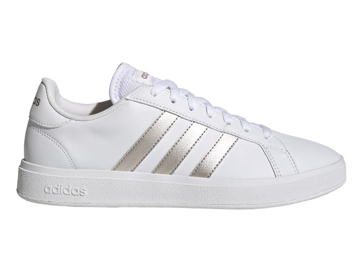 Tenis Adidas blancos con franjas laterales en color plata metálico y suela blanca.