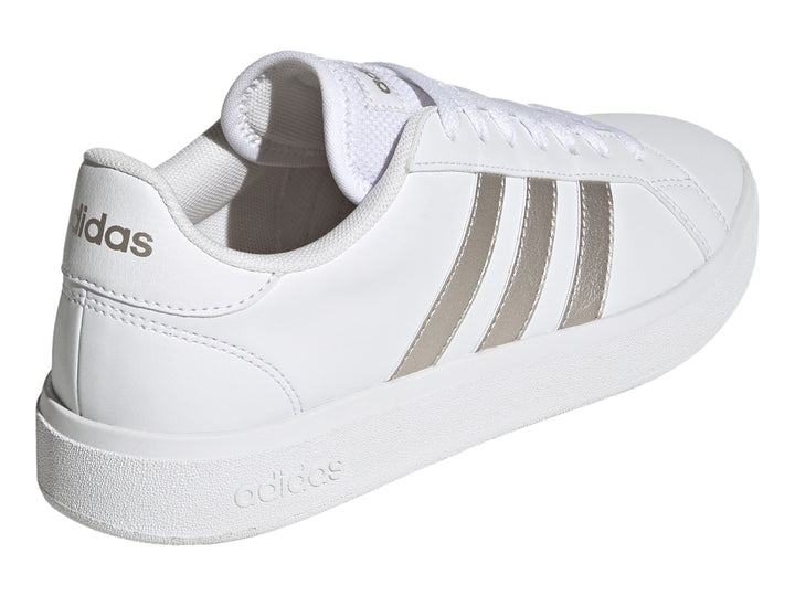 Tenis Adidas blancos con franjas laterales en color plata metálico y suela blanca.