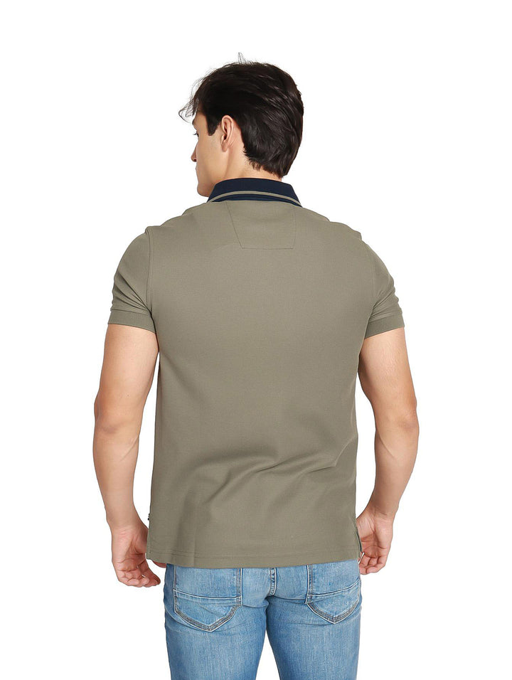 Hombre vistiendo playera polo Nautica color verde oliva con cuello azul marino y jeans azules.