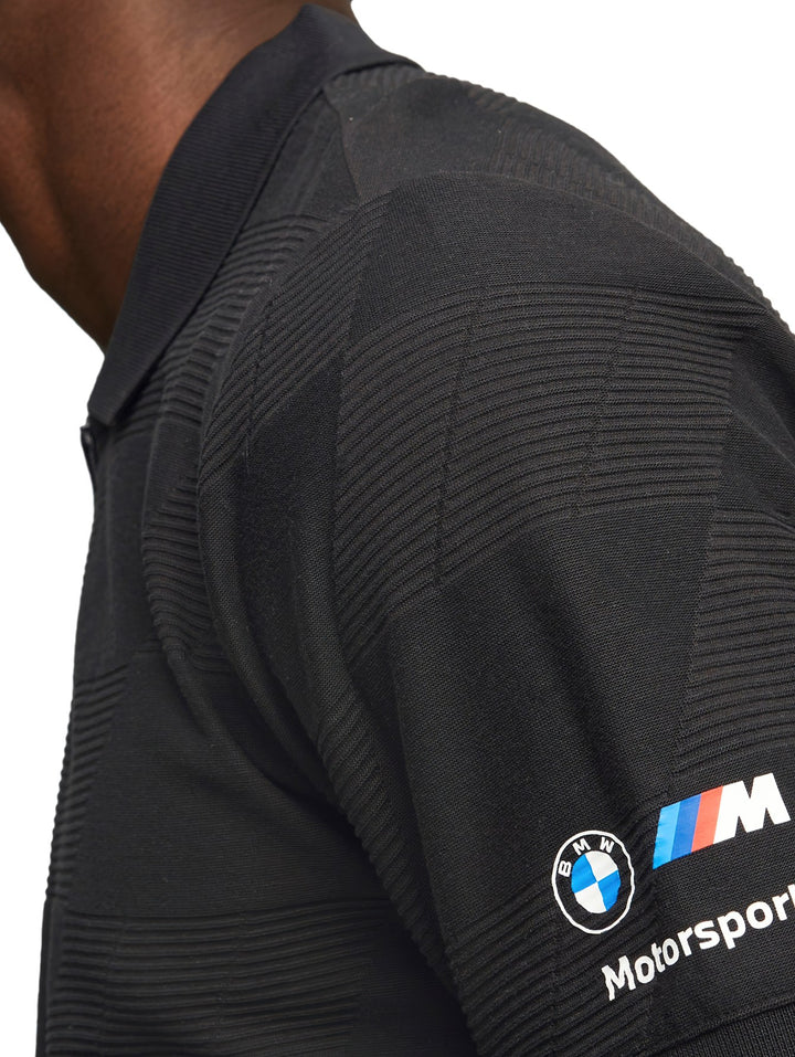 Hombre vistiendo una polo PUMA BMW MMS de color negro con textura jacquard y logos en la manga.