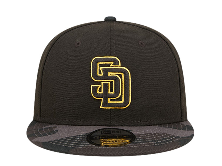 Gorra New Era negra con logo bordado en dorado y visera con estampado de camuflaje oscuro.