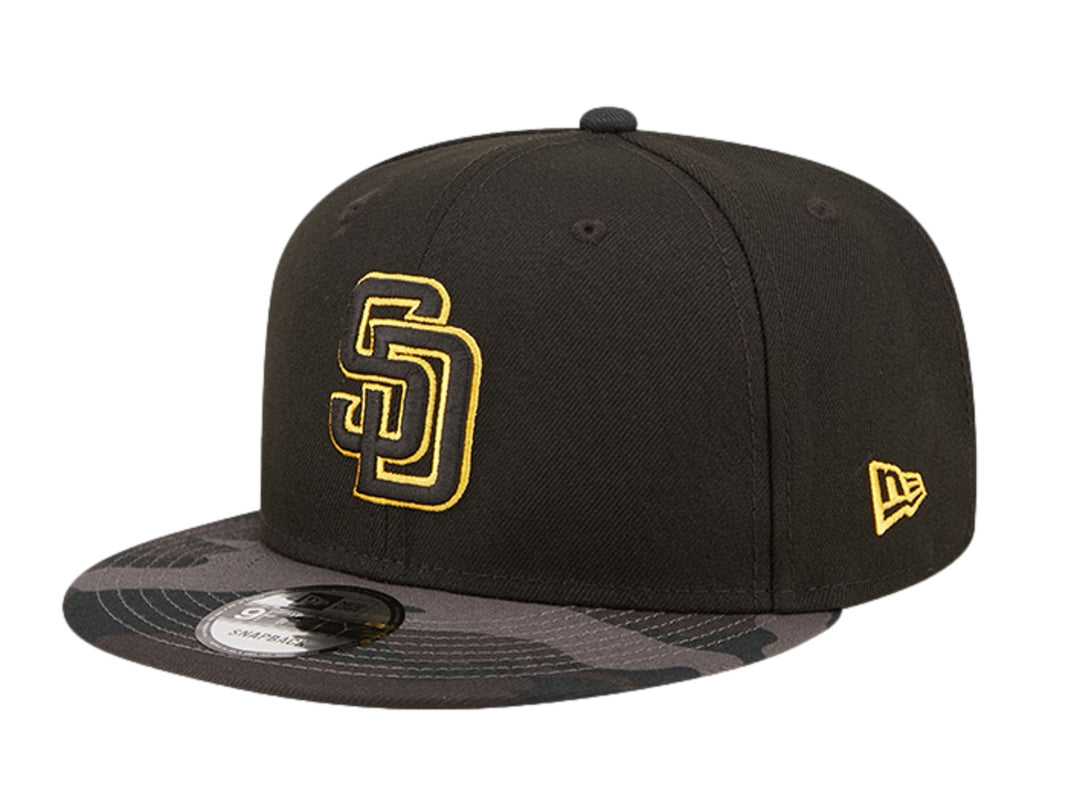 Gorra New Era negra con logo bordado en dorado y visera con estampado de camuflaje oscuro.
