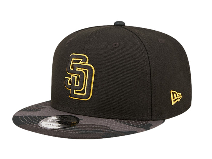 Gorra New Era negra con logo bordado en dorado y visera con estampado de camuflaje oscuro.