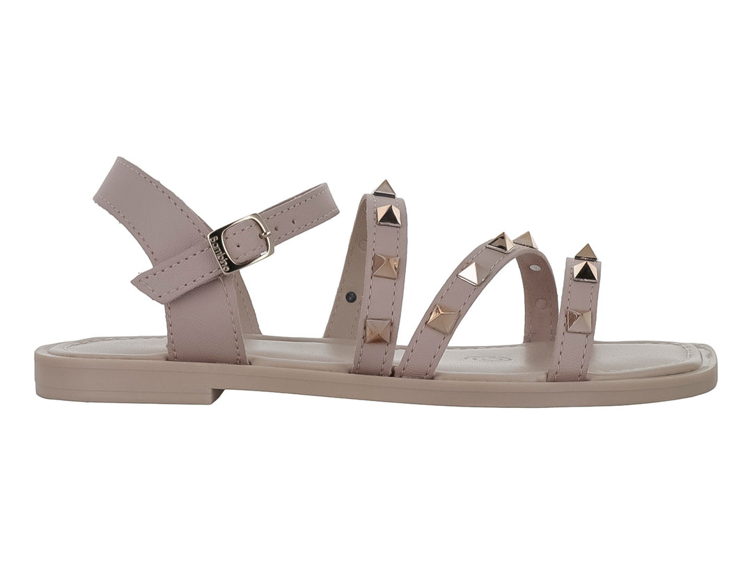 Sandalia plana color beige para niña con tiras decoradas con tachuelas doradas y cierre de hebilla.