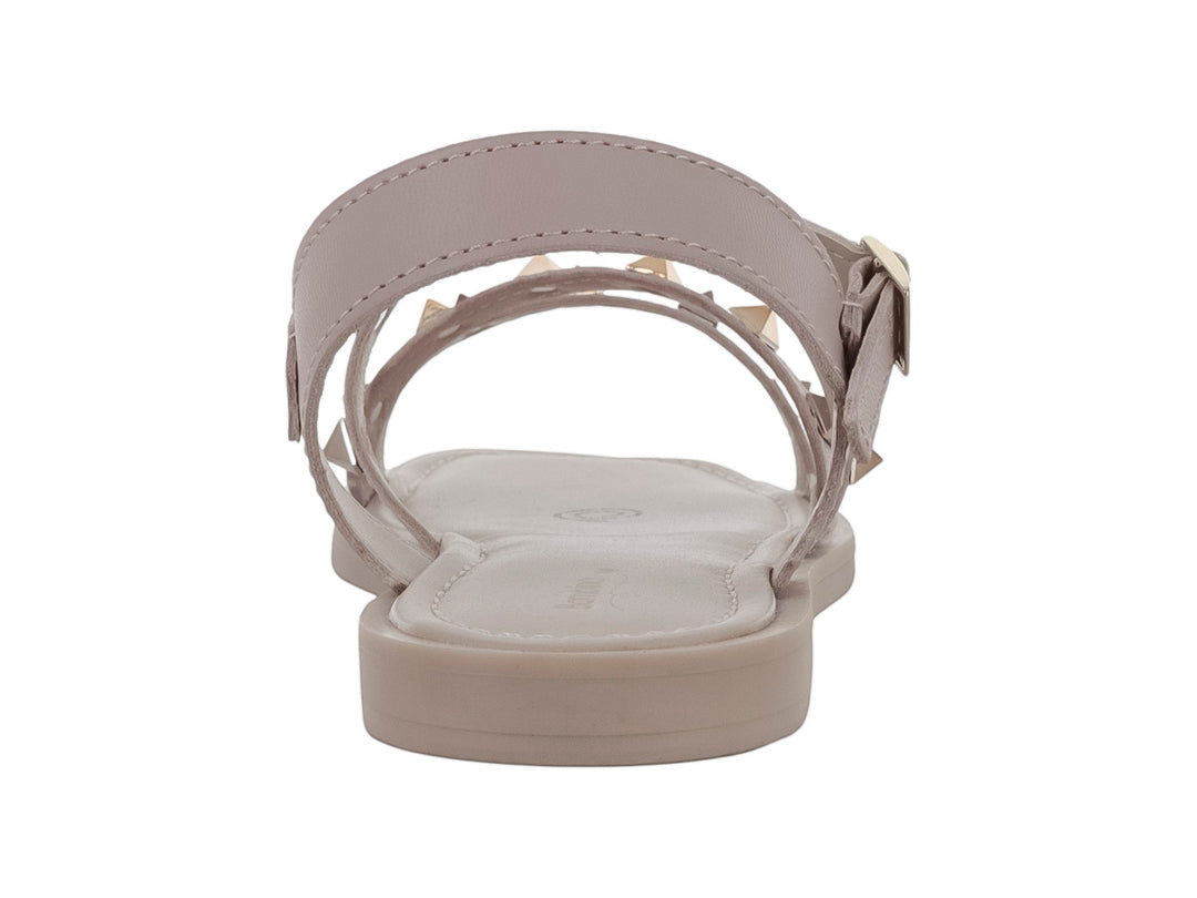 Sandalia plana color beige para niña con tiras decoradas con tachuelas doradas y cierre de hebilla.
