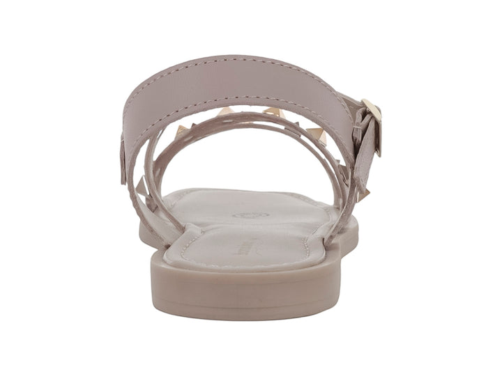 Sandalia plana color beige para niña con tiras decoradas con tachuelas doradas y cierre de hebilla.