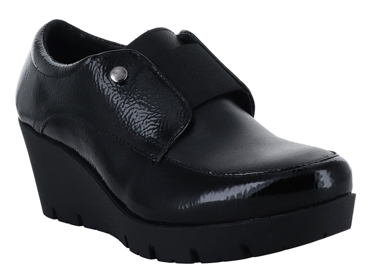 Zapato de piel negro con plataforma alta, acabado brillante y correa frontal con botón decorativo.