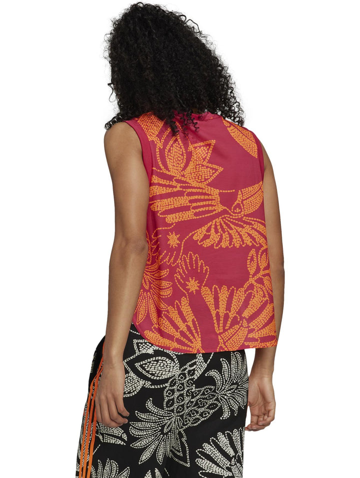 Mujer vistiendo camiseta Adidas sin mangas color Vivid Berry y naranja con estampado floral y pantalones a juego.