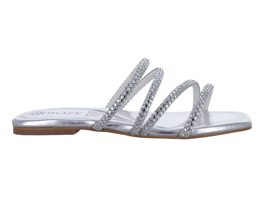 Sandalia plana color plata para niña con tiras decoradas con brillos brillantes.