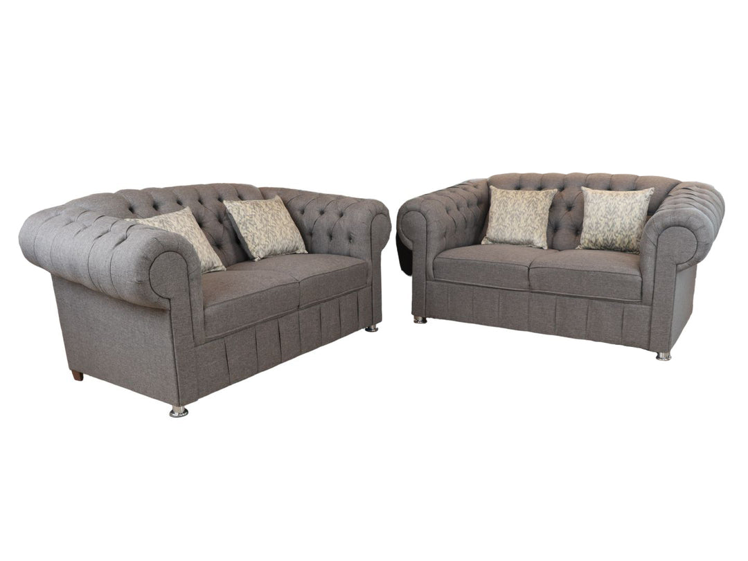 Juego de sala compuesto por dos sofás grises estilo Chesterfield con capitoné y cojines decorativos.