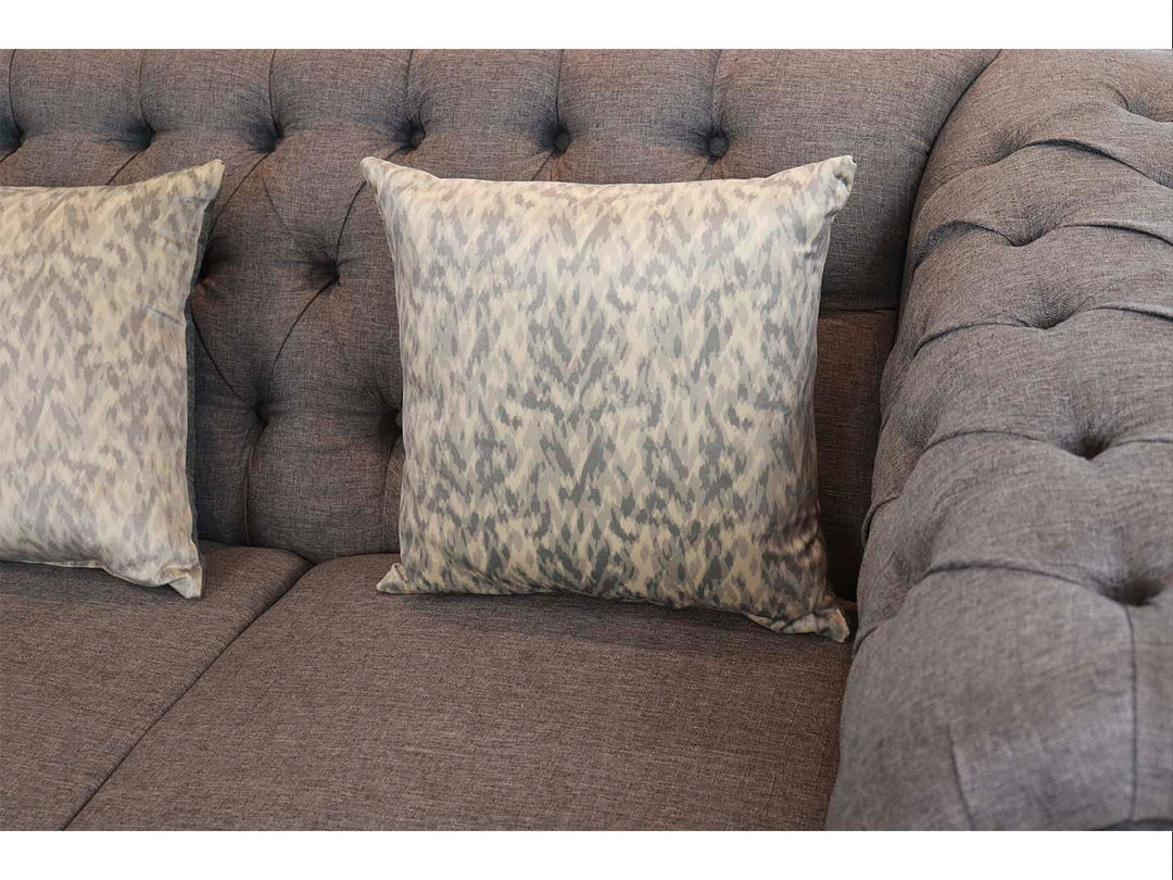 Juego de sala compuesto por dos sofás grises estilo Chesterfield con capitoné y cojines decorativos.