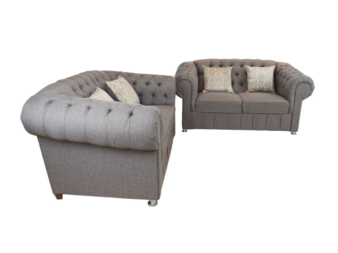 Juego de sala compuesto por dos sofás grises estilo Chesterfield con capitoné y cojines decorativos.