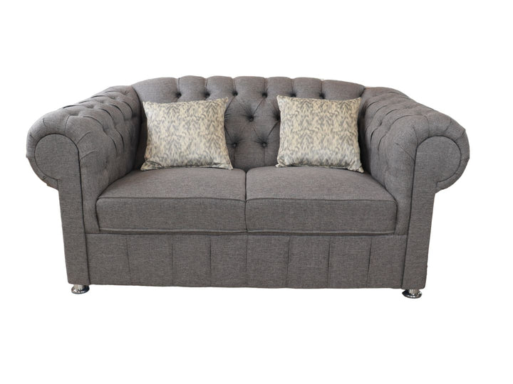 Juego de sala compuesto por dos sofás grises estilo Chesterfield con capitoné y cojines decorativos.