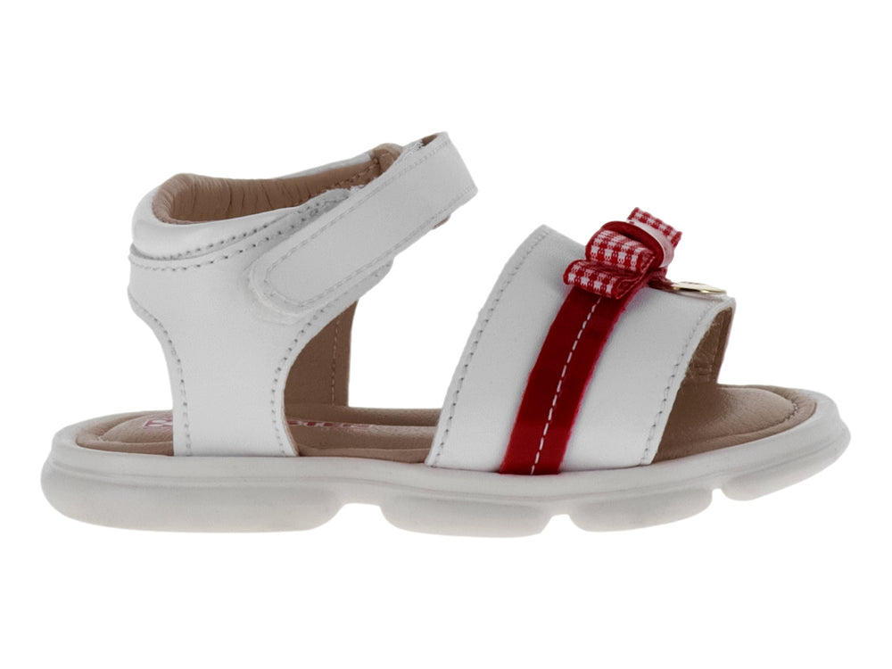 Sandalia blanca para niña con detalle de moño rojo y correa ajustable en el tobillo.