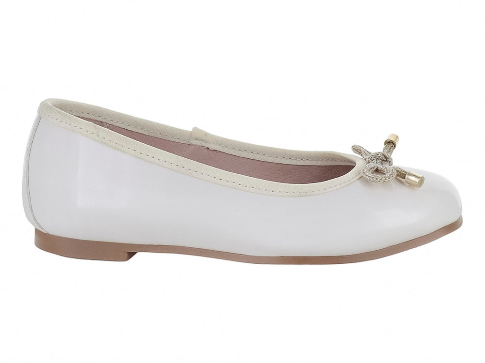 Zapato tipo balerina color hueso con acabado brillante y detalle de moño dorado en la punta para niña.