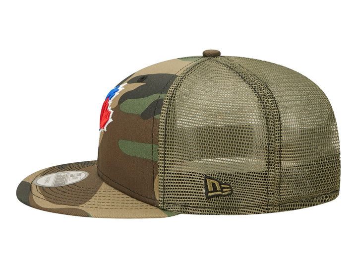 Gorra New Era con estampado de camuflaje en tonos verdes y cafés, visera plana y logo bordado al frente.
