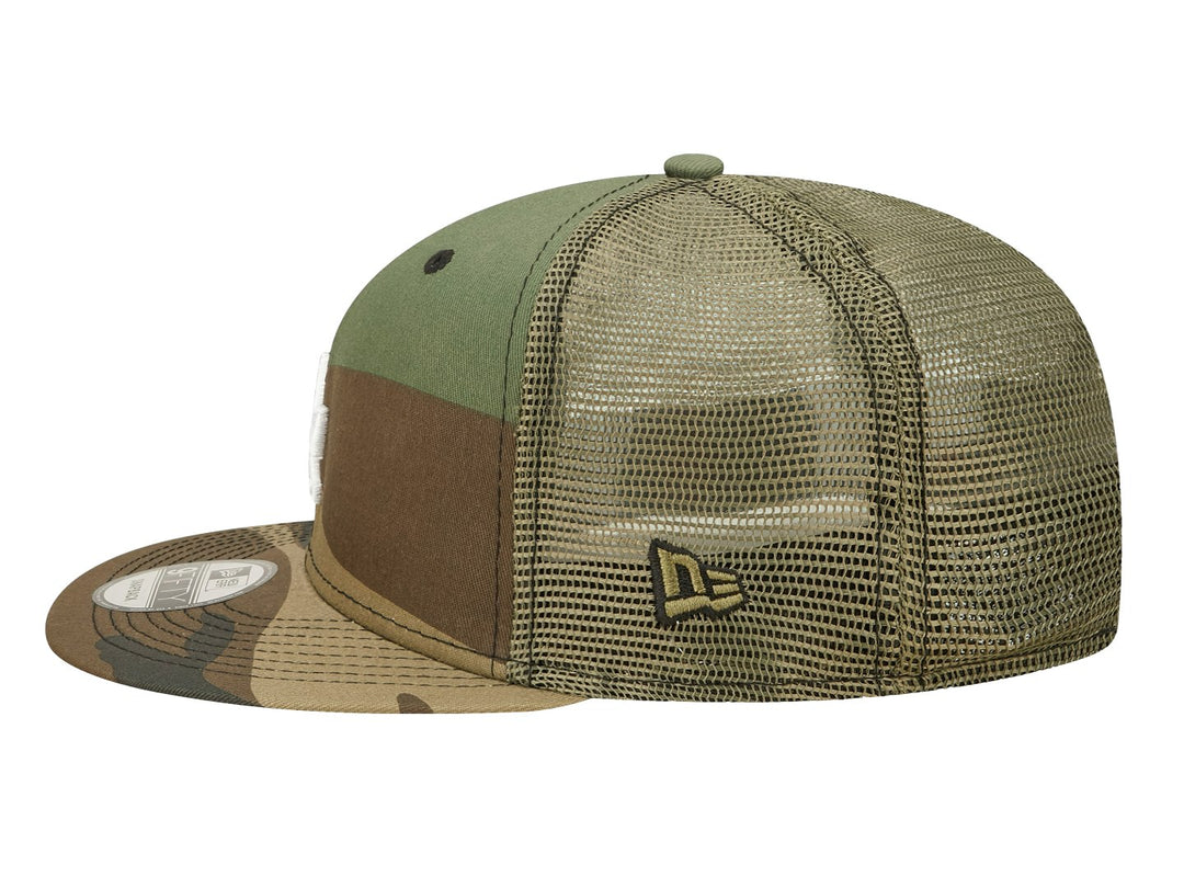 Gorra New Era con estampado de camuflaje en tonos verdes y cafés, visera plana y logo LA bordado en blanco.