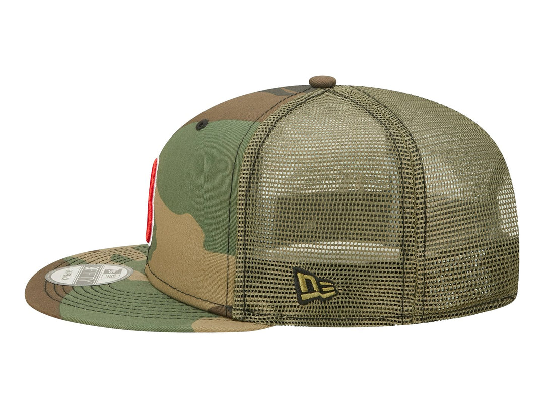 Gorra New Era estilo trucker con estampado de camuflaje y logotipo bordado en rojo y blanco al frente.