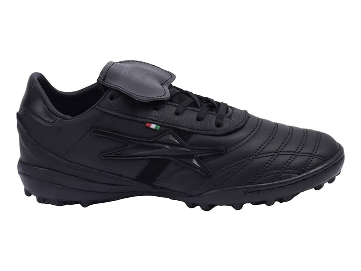Zapato de fútbol negro con lengüeta plegable y suela para césped sintético.