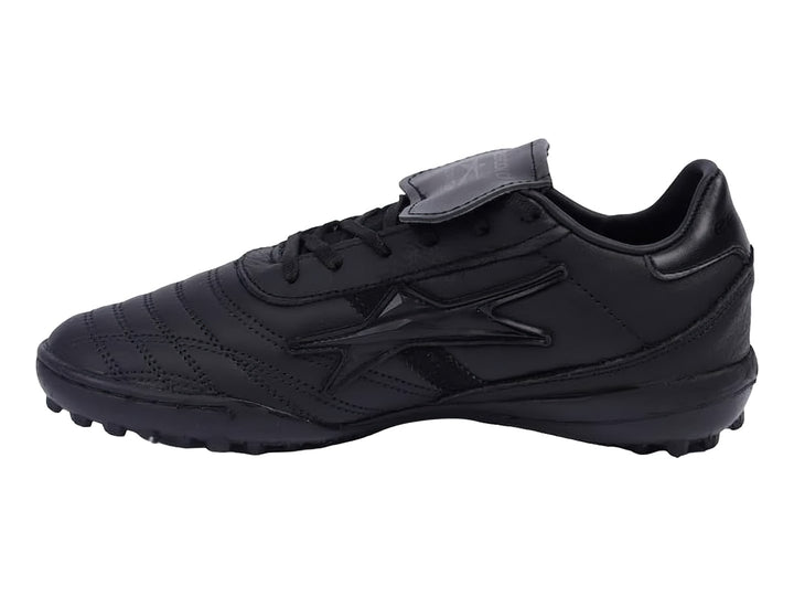 Zapato de fútbol negro con lengüeta plegable y suela para césped sintético.