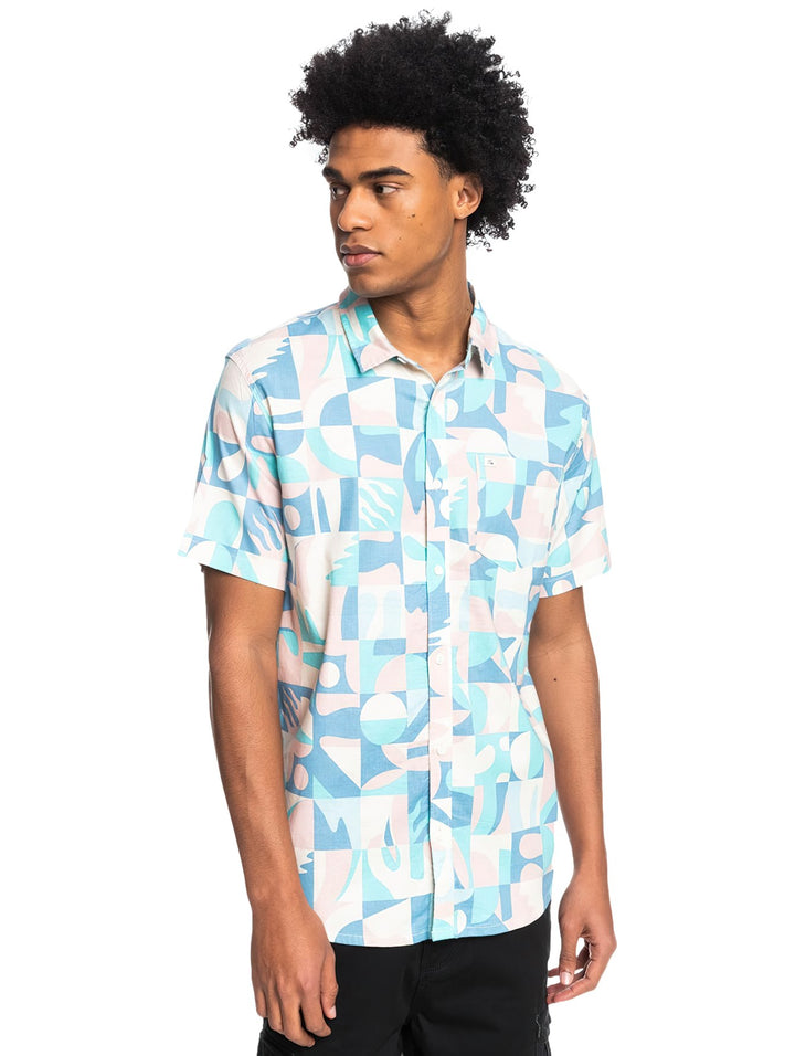 Hombre vistiendo camisa Quiksilver de manga corta con estampado geométrico en tonos azul, blanco y rosa pastel.