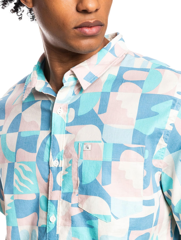 Hombre vistiendo camisa Quiksilver de manga corta con estampado geométrico en tonos azul, blanco y rosa pastel.