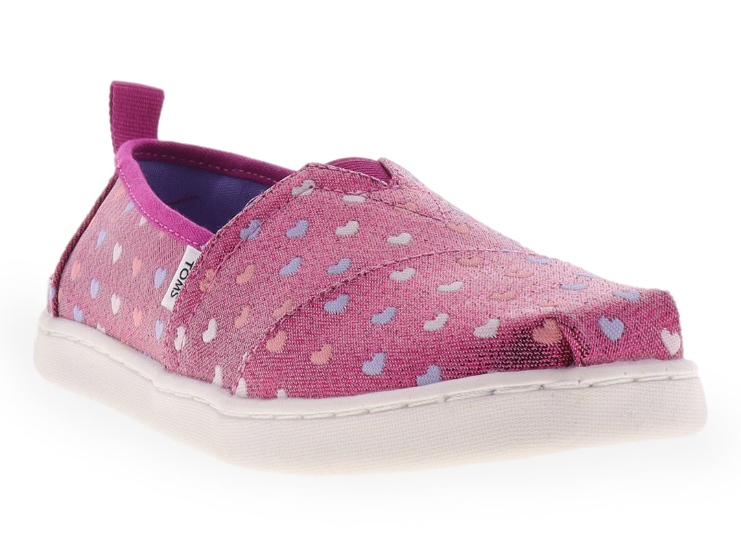 Zapato slip-on TOMS color fucsia brillante con estampado de corazones multicolores y suela blanca.