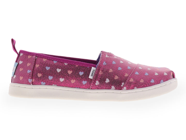 Zapato slip-on TOMS color fucsia brillante con estampado de corazones multicolores y suela blanca.