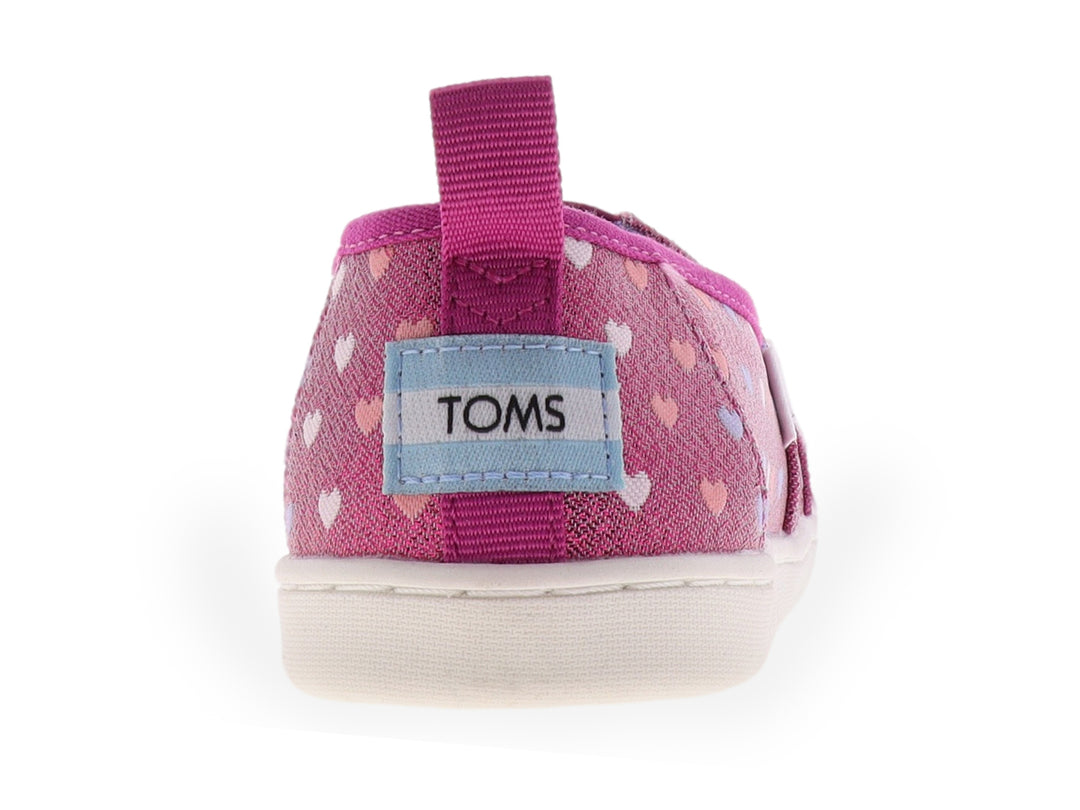 Zapato slip-on TOMS color fucsia brillante con estampado de corazones multicolores y suela blanca.