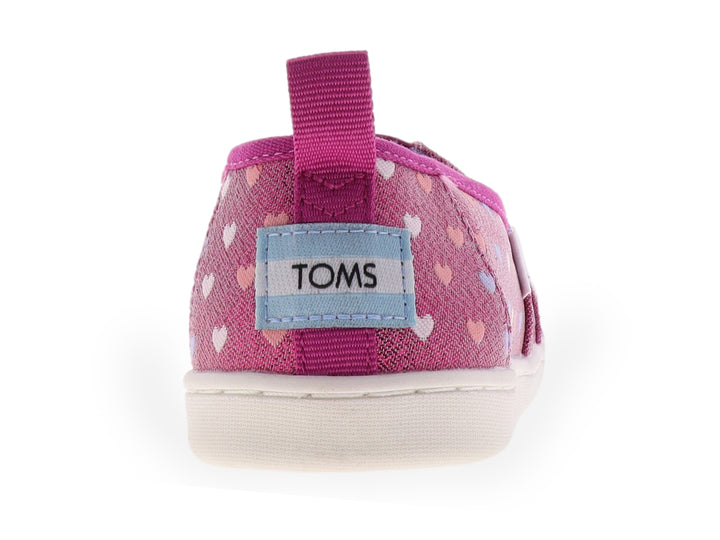 Zapato slip-on TOMS color fucsia brillante con estampado de corazones multicolores y suela blanca.