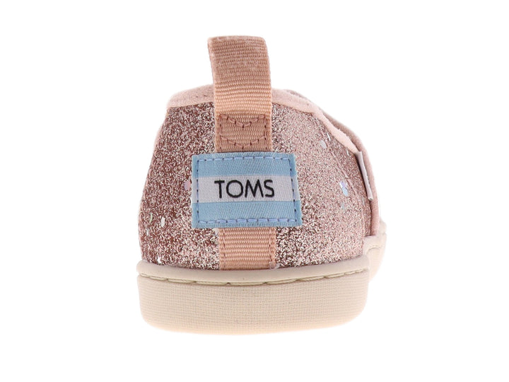 Zapato slip-on TOMS color oro rosa con acabado brillante y suela color crema.