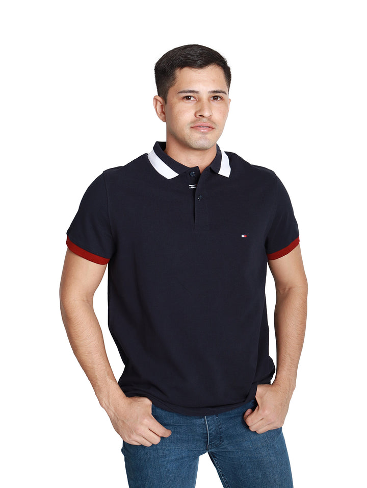 Hombre vistiendo polo Tommy Hilfiger azul marino con cuello blanco y detalles rojos en las mangas.