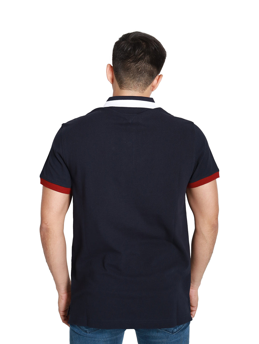 Hombre vistiendo polo Tommy Hilfiger azul marino con cuello blanco y detalles rojos en las mangas.