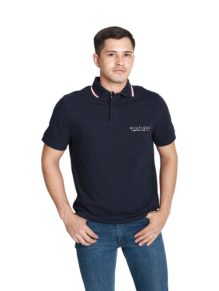 Hombre vistiendo una camiseta polo azul marino de manga corta con detalles en el cuello y logo en el pecho.