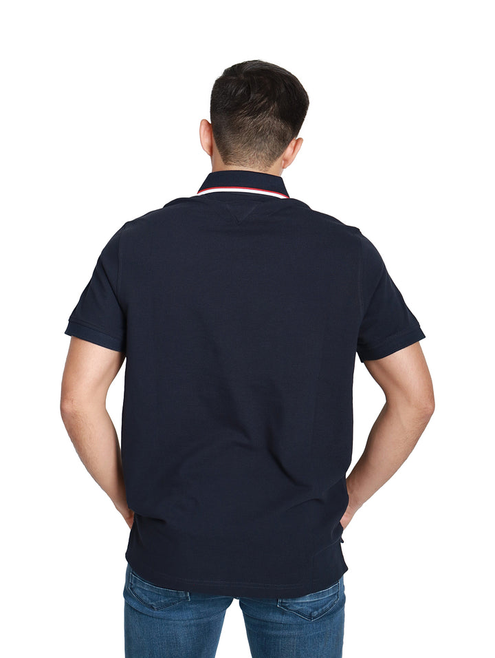 Hombre vistiendo una camiseta polo azul marino de manga corta con detalles en el cuello y logo en el pecho.