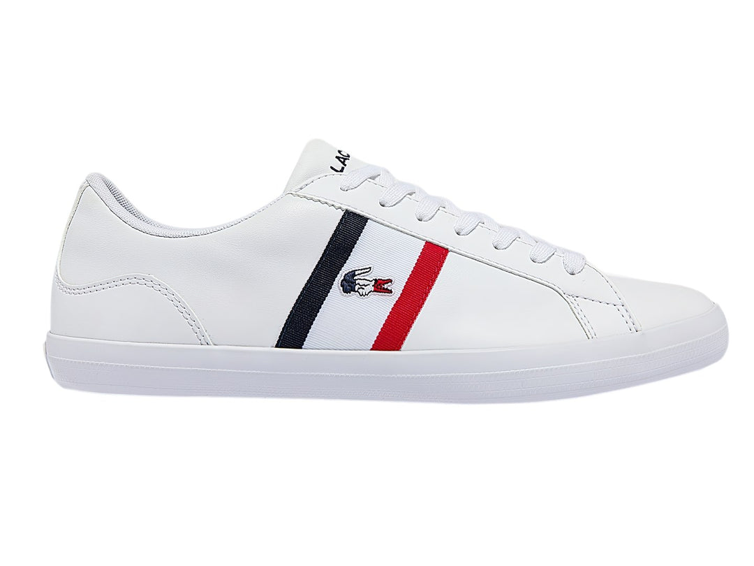 Tenis blancos Lacoste de corte bajo con franjas azul marino y rojo en el lateral y logotipo del cocodrilo.