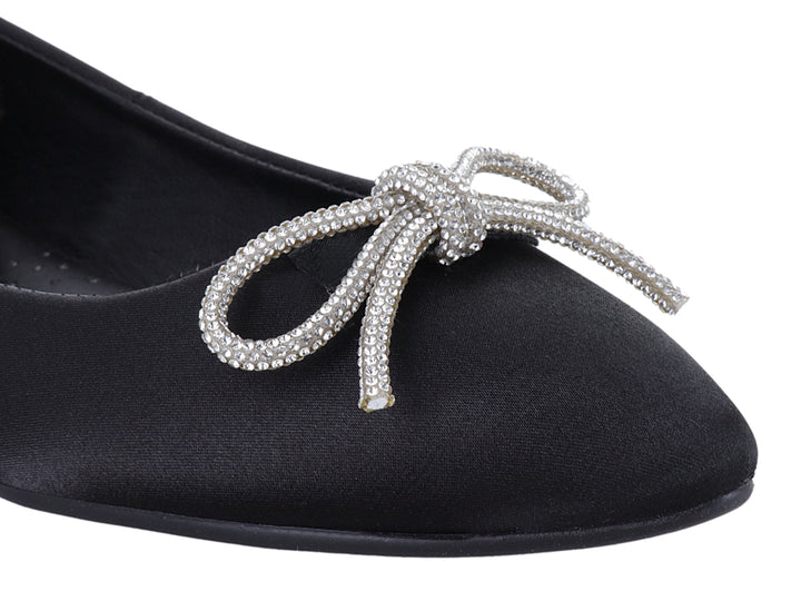 Zapato plano negro de material brillante con un moño decorativo de pedrería plateada en la punta.