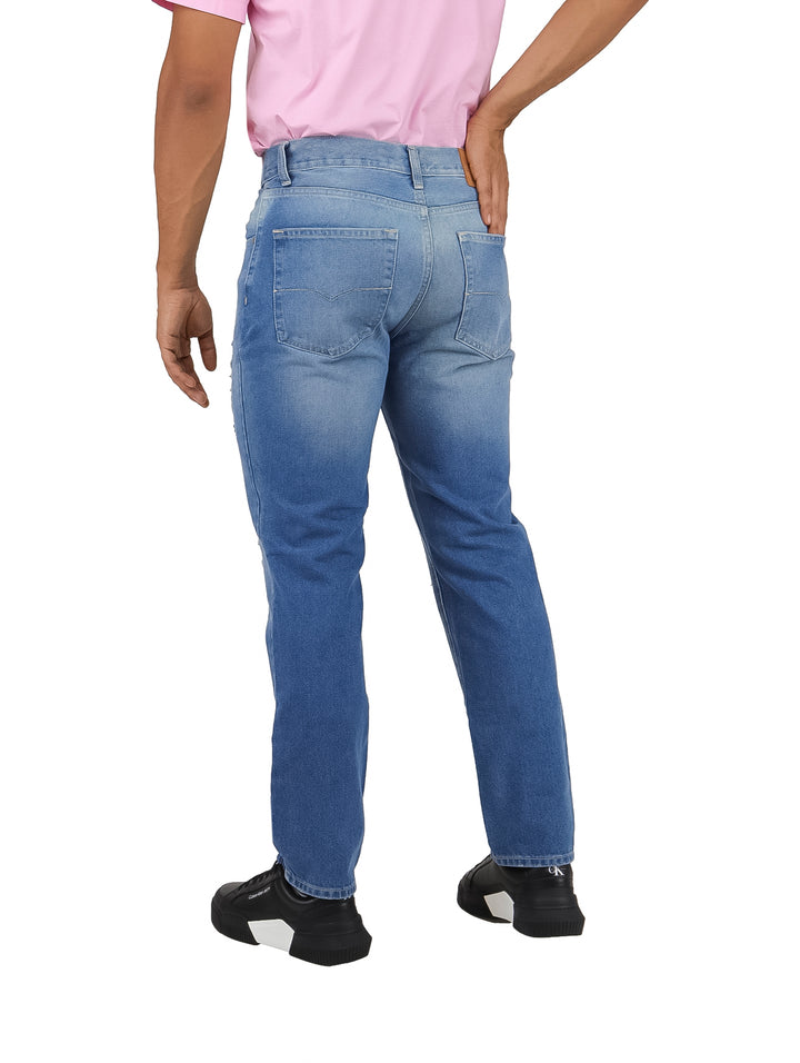 Pantalones jeans azules para hombre con efecto lavado y detalles rotos en las piernas.