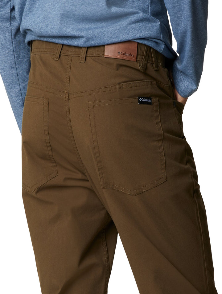 Hombre vistiendo pantalones Columbia color verde oliva, camiseta azul y calzado deportivo.