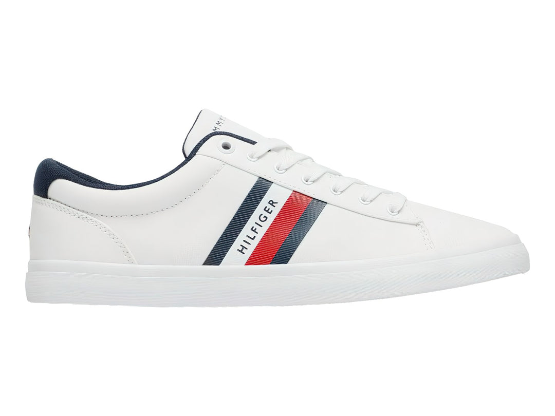 Tenis Tommy Hilfiger color blanco con franjas azul y roja en el lateral y suela blanca.