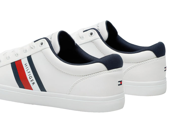 Tenis Tommy Hilfiger color blanco con franjas azul y roja en el lateral y suela blanca.