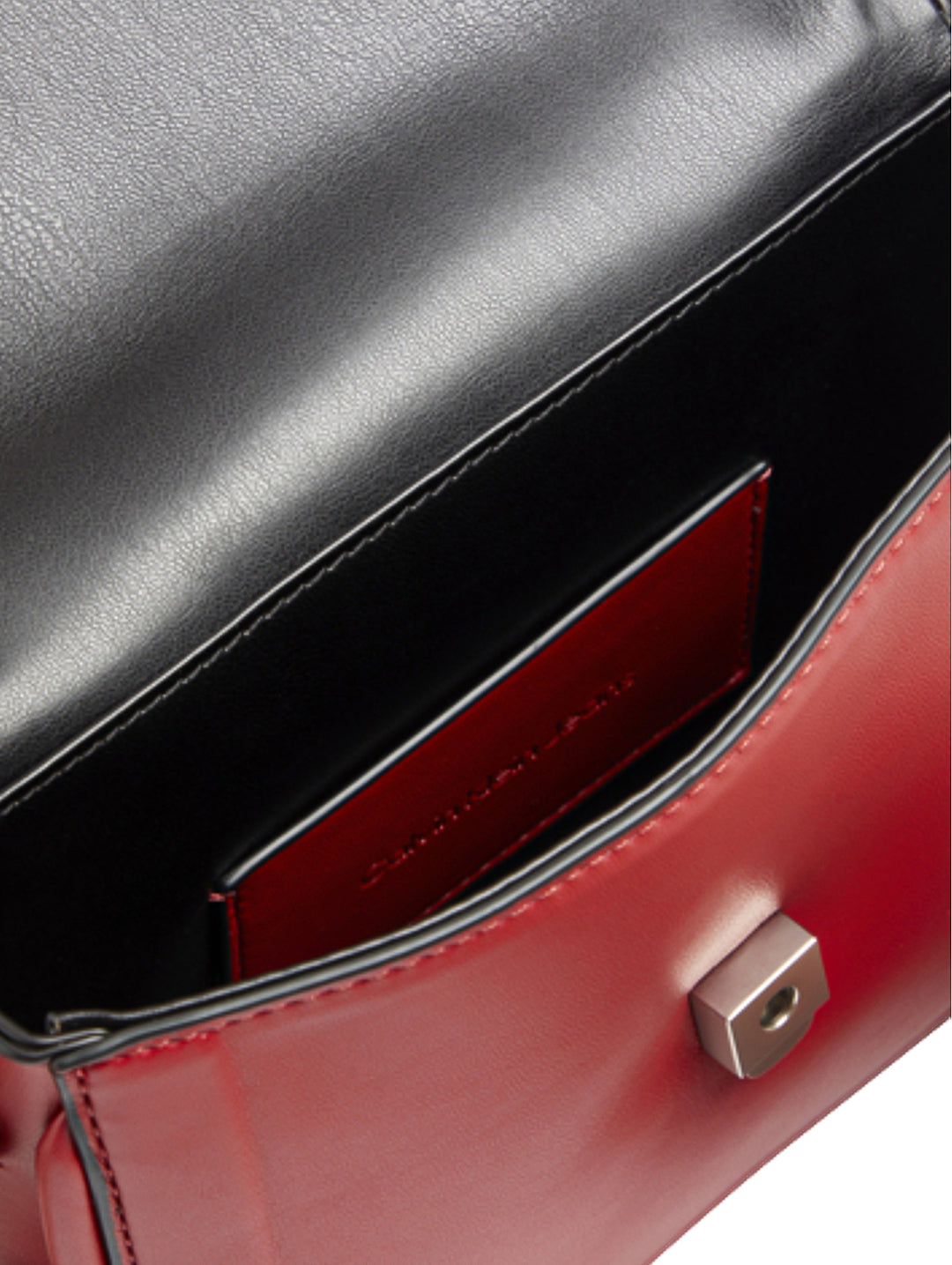 Bolso rojo de Calvin Klein con asa superior, correa ajustable y logo CK grabado en relieve.