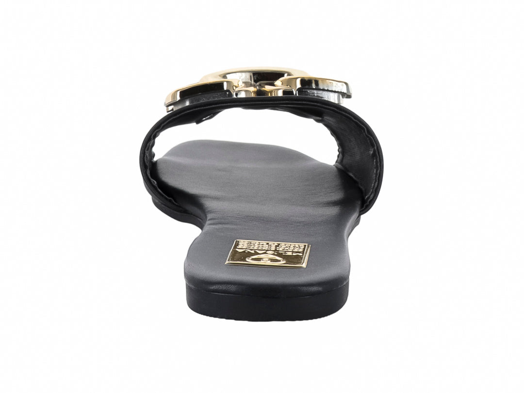 Sandalia plana color negro con un adorno metálico dorado en la parte superior.