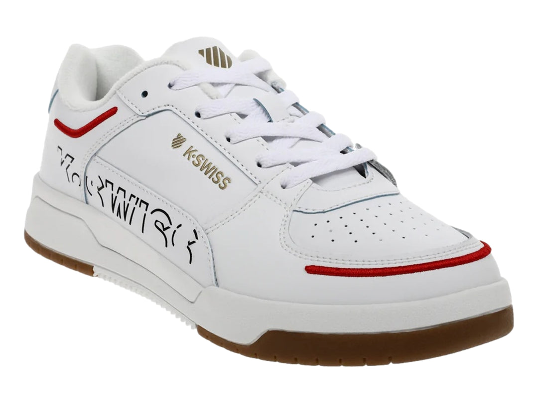 Tenis K-Swiss blancos con suela de goma marrón y detalles decorativos en rojo y negro.