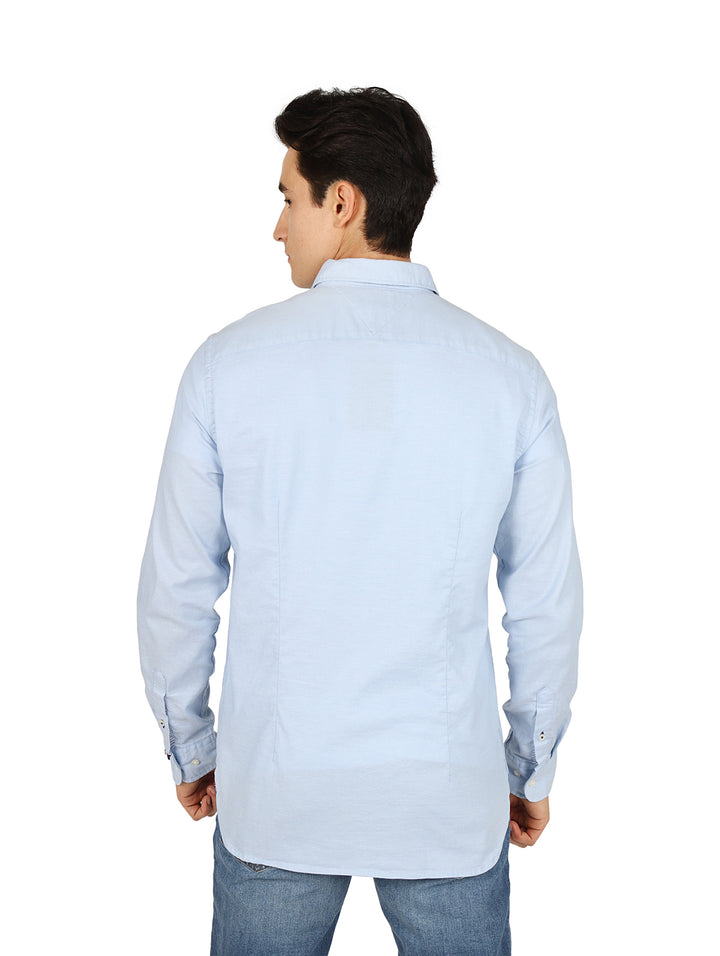Hombre vistiendo una camisa Tommy Hilfiger de color azul claro con botones y manga larga.