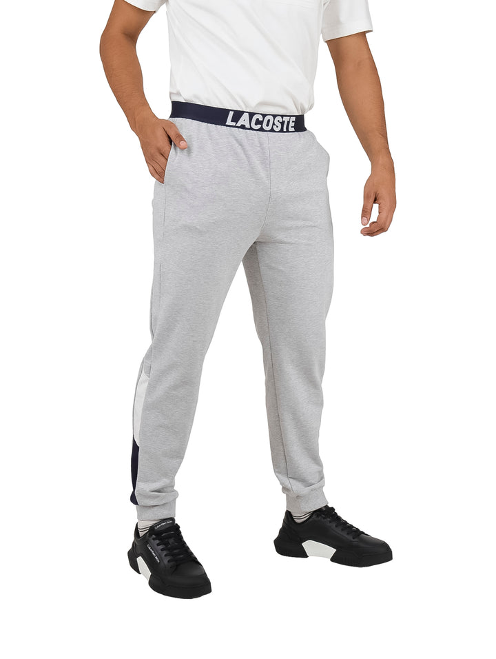 Hombre vistiendo pantalón de pijama gris de Lacoste con cintura elástica azul marino.